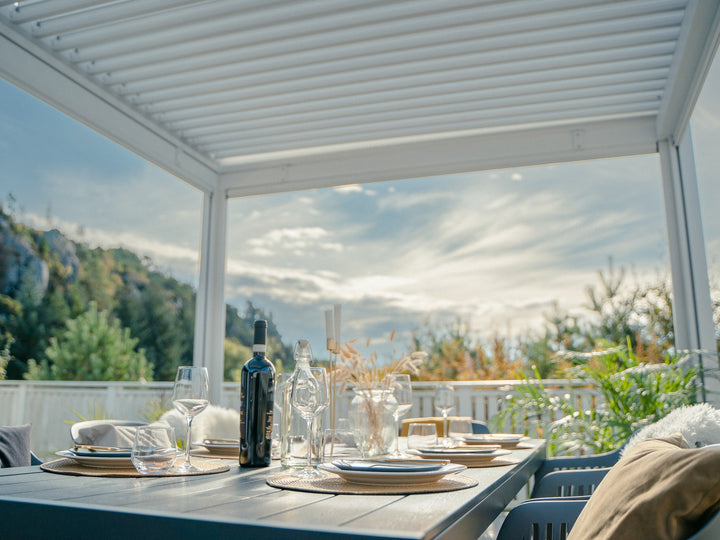 Pergolux Pergola 3x4, hvit, frittstående med hvite screens på en lys terrasse. Middagsbordet er dekket klart